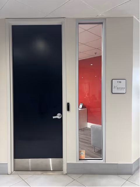 Interior hallway with a dark door, glass panel, and BAYADA Assistive Care sign.