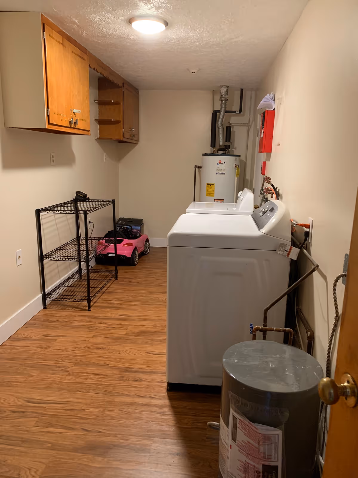 Interior utility room with washer, dryer, cabinets, water heater, and plastic toy car.