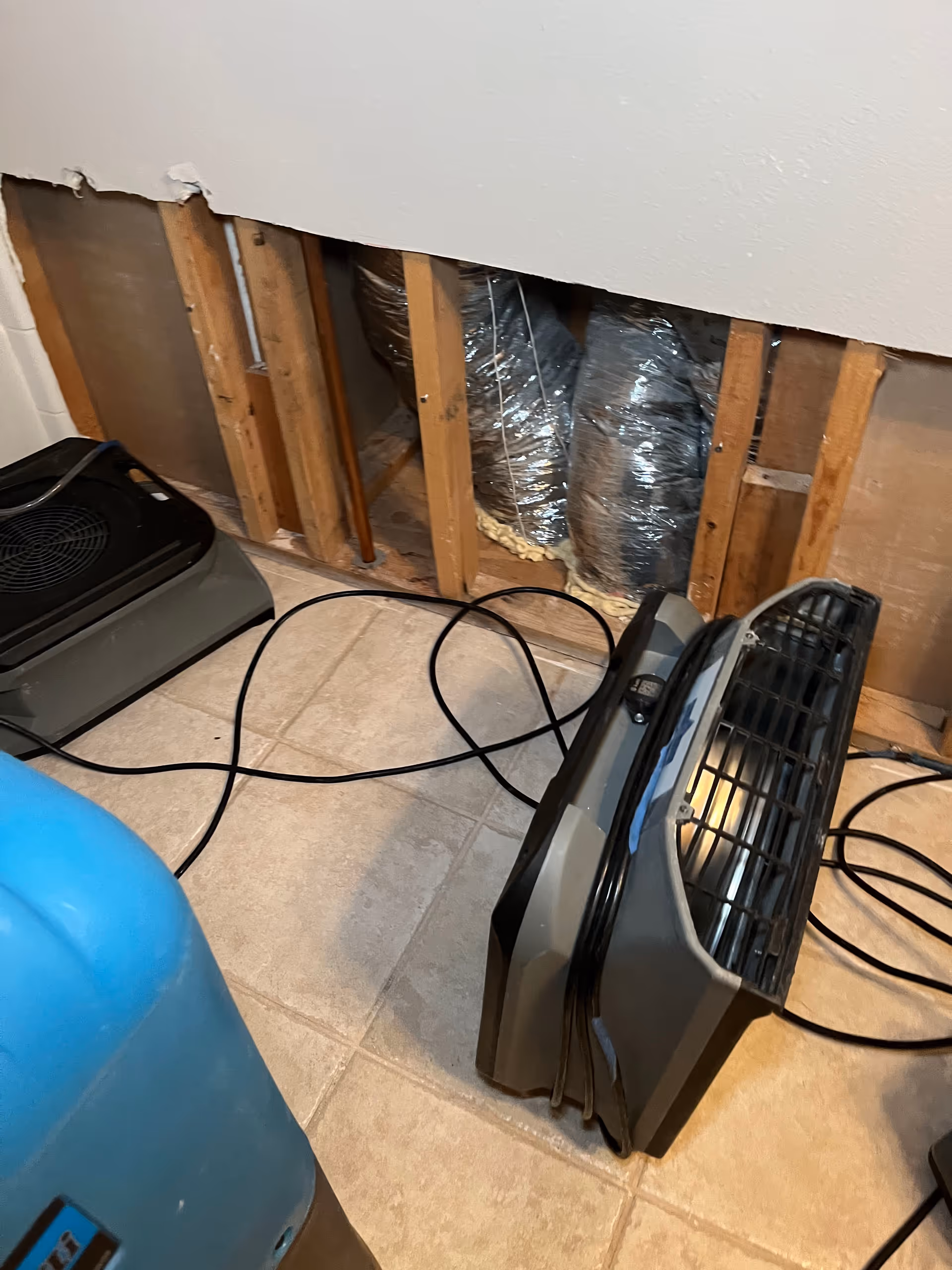 Unfinished interior wall with exposed studs, ductwork, heater, and tangled cables on tile floor