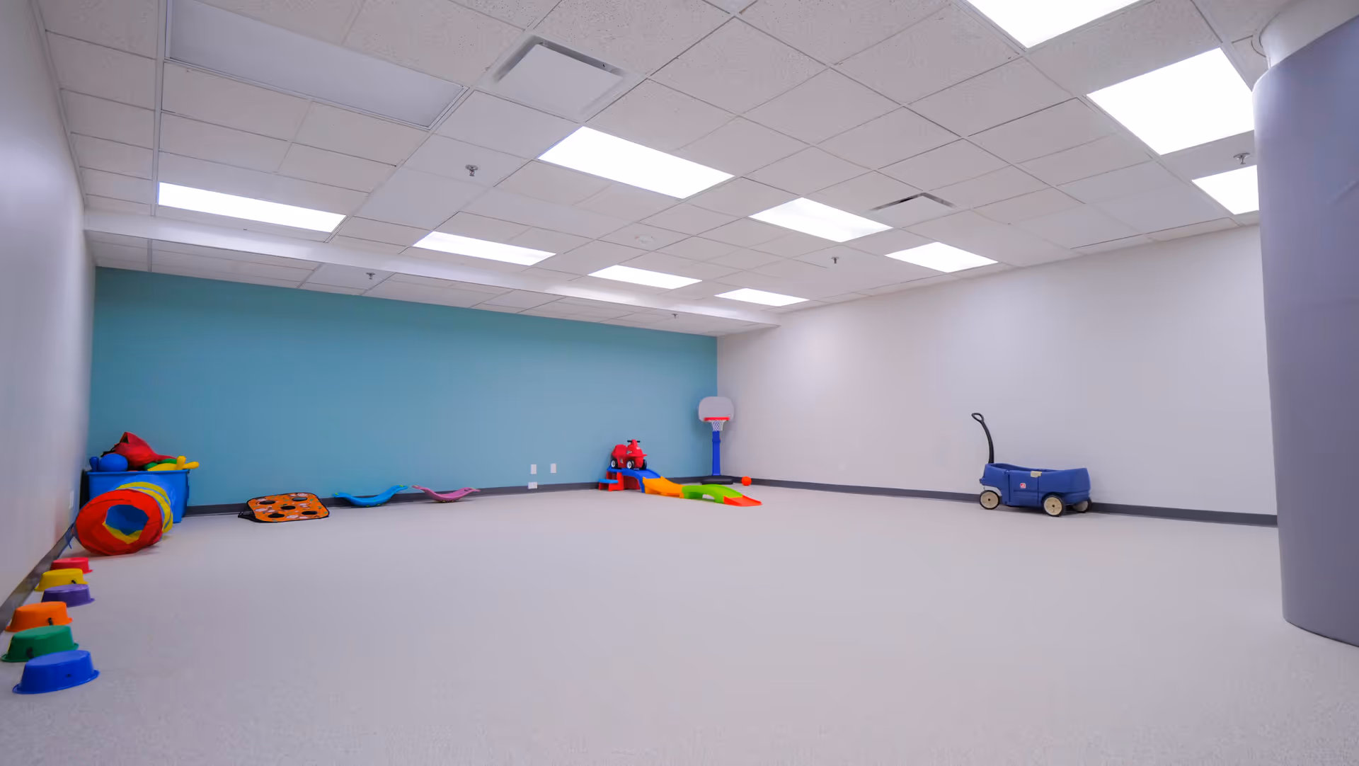 Empty therapy playroom with colorful toys along a blue accent wall and bright ceiling lights.