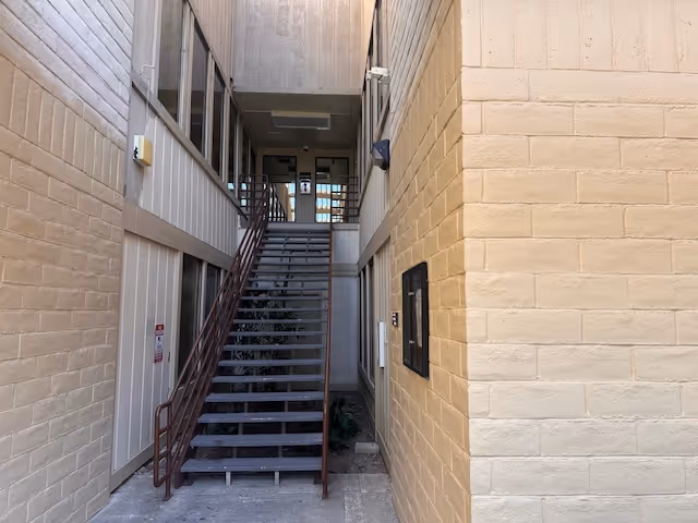 A stairwell between beige brick walls leads up to a hallway in a senior living facility.