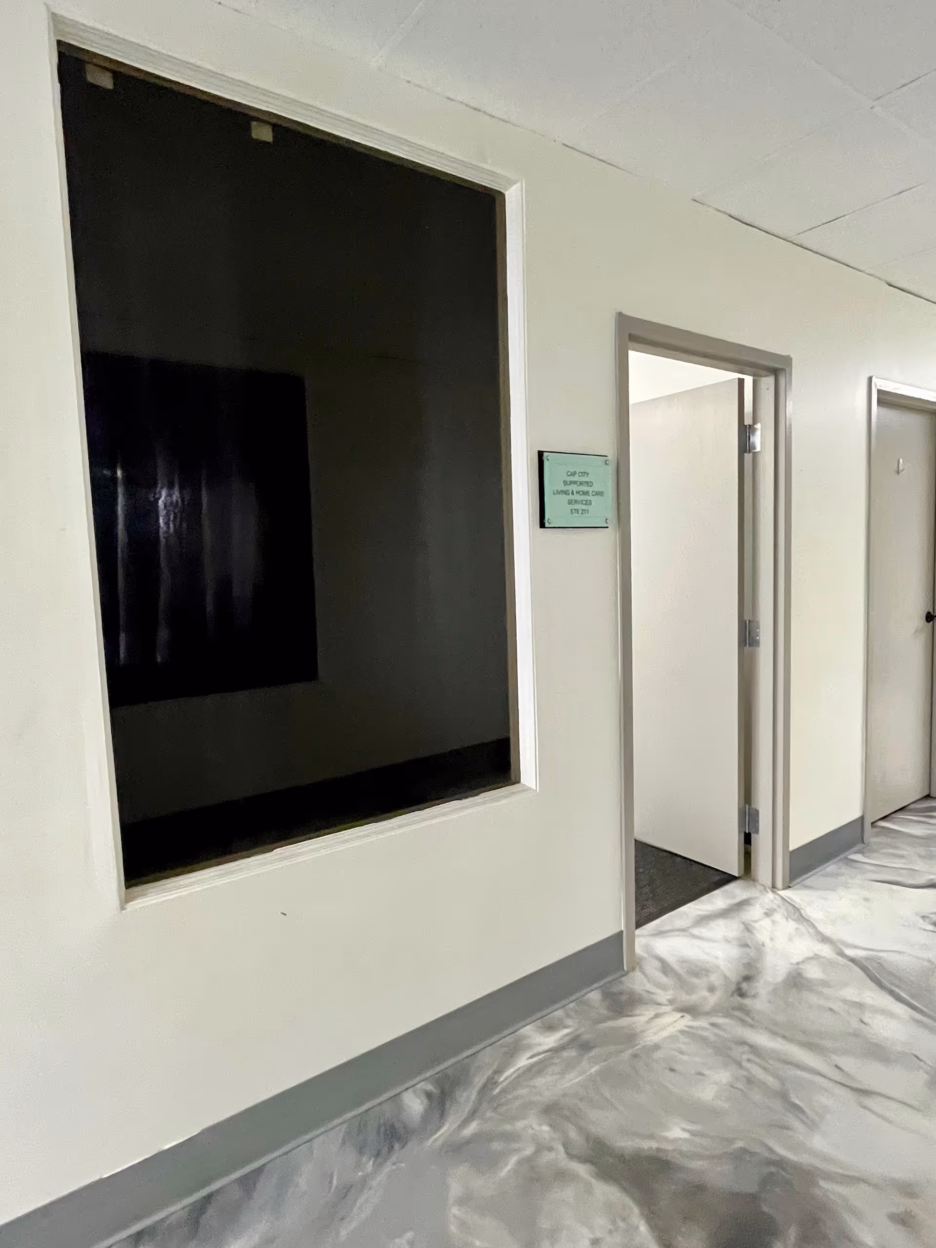 Interior hallway of Cap City Supported Living with an open door and dark display window.