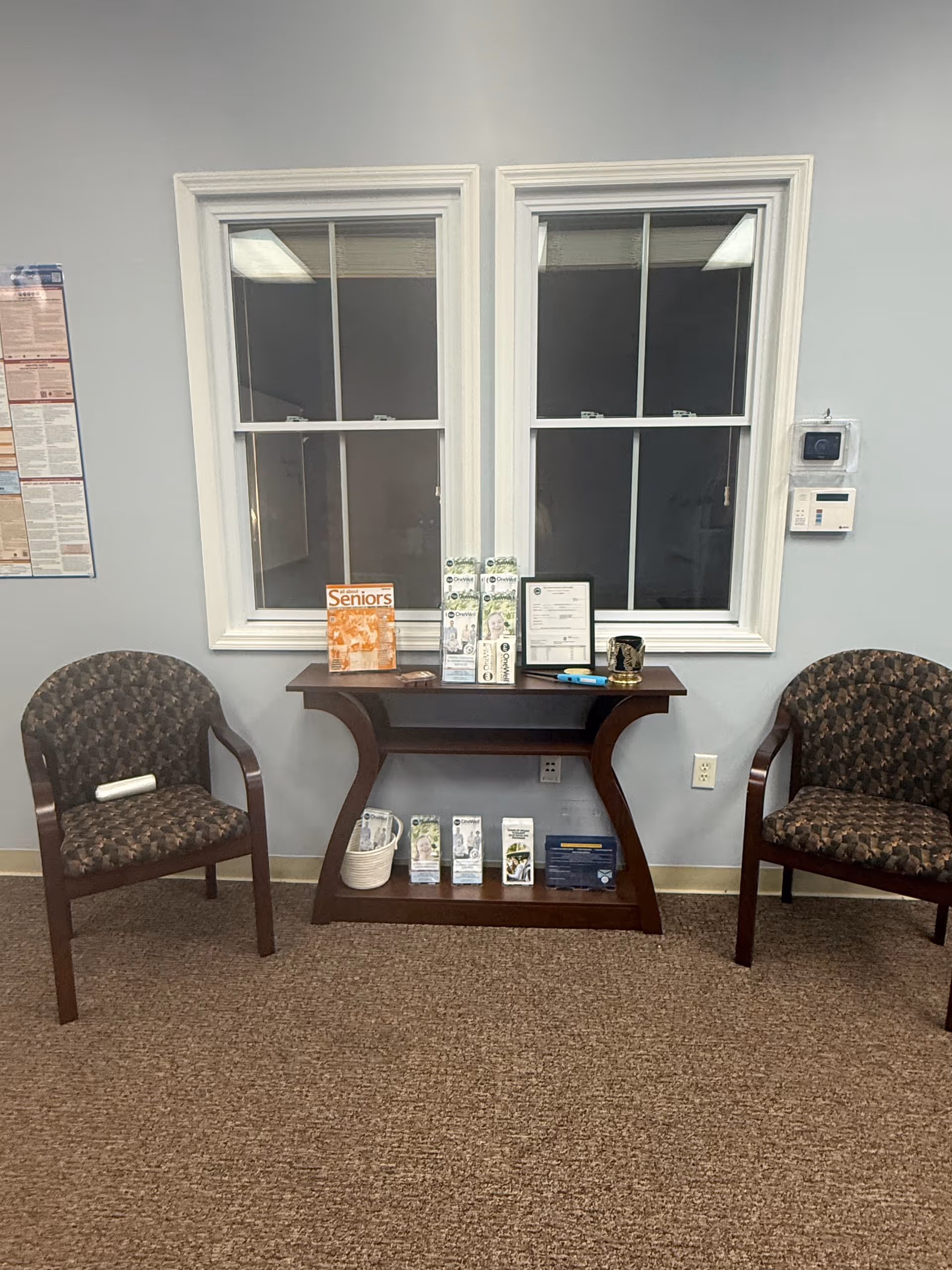 Two upholstered chairs frame a dark wood console with brochures by windows.