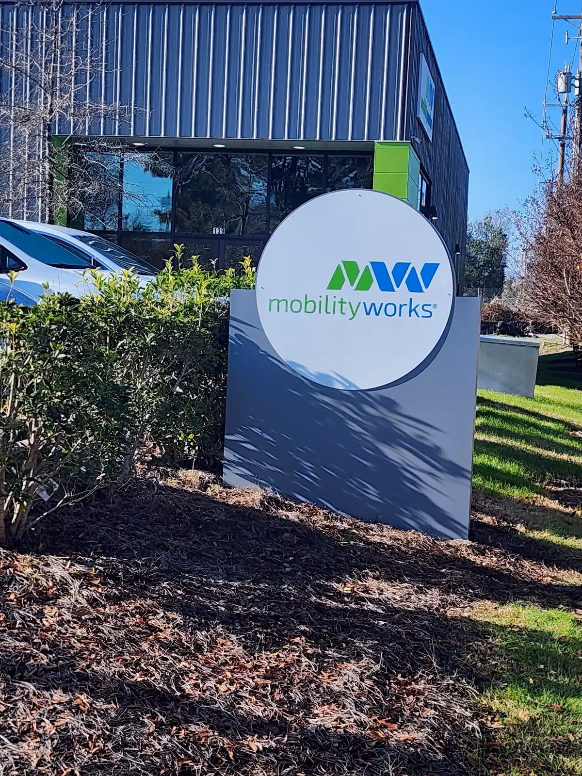 Exterior view of MobilityWorks facility with a circular sign and surrounding landscaping.