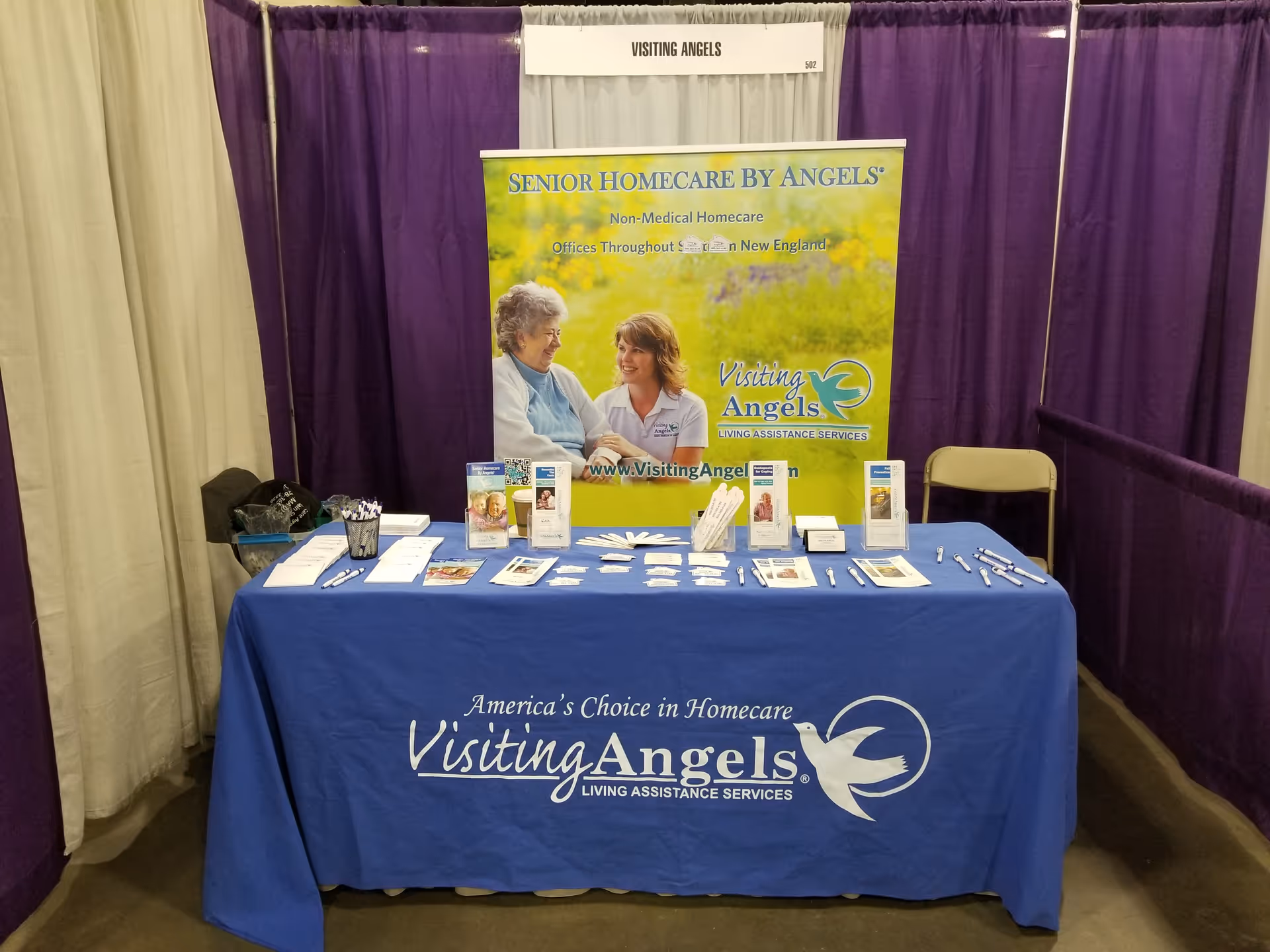 Indoor expo booth for Visiting Angels Senior Home Care with a blue table and banner.