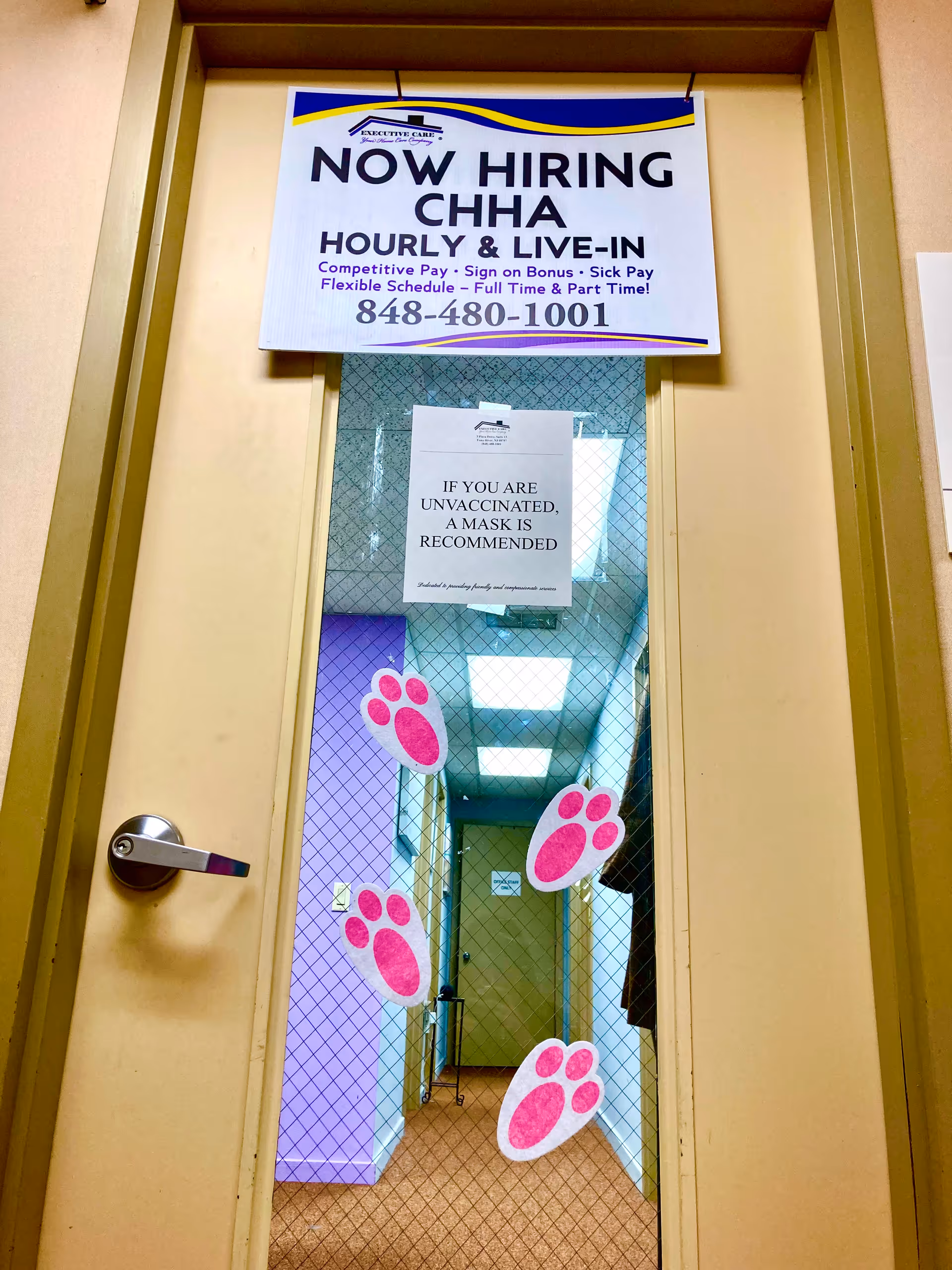 Doorway with a Now Hiring CHHA sign, pink paw prints on glass, hallway beyond.