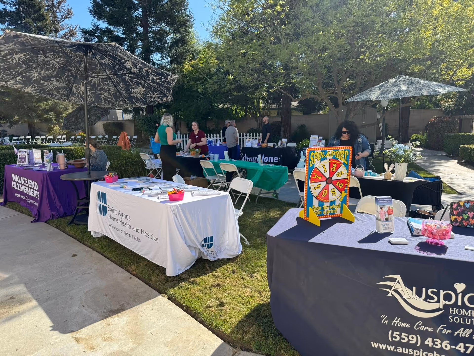 Outdoor senior care fair with booths and people under umbrellas.