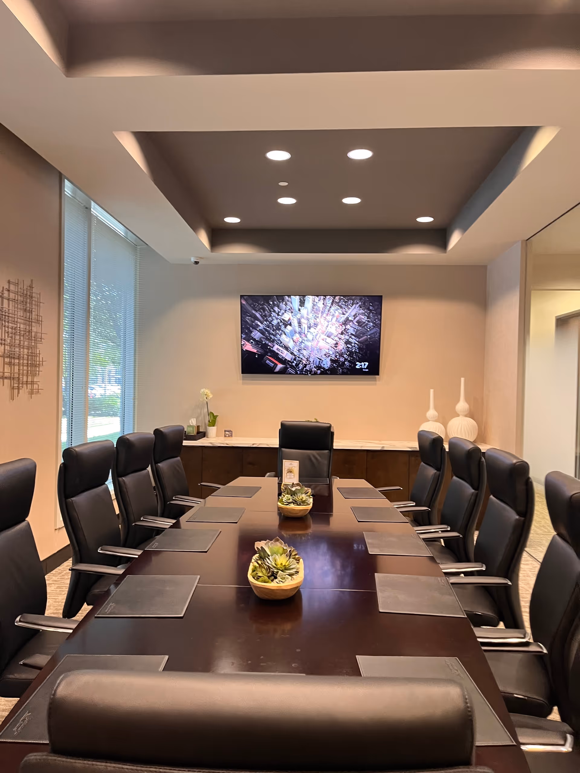 A modern conference room with a long dark wood table, chairs, and a wall mounted TV.