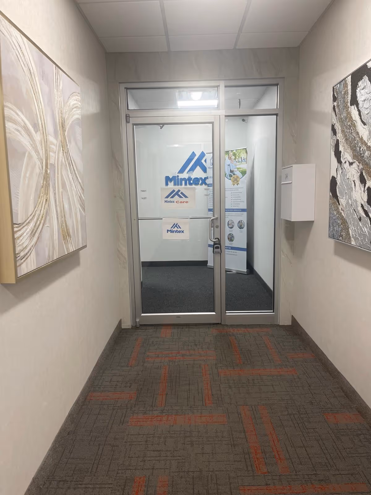 Indoor hallway leading to glass doors with Mintex Care signage and patterned carpet.