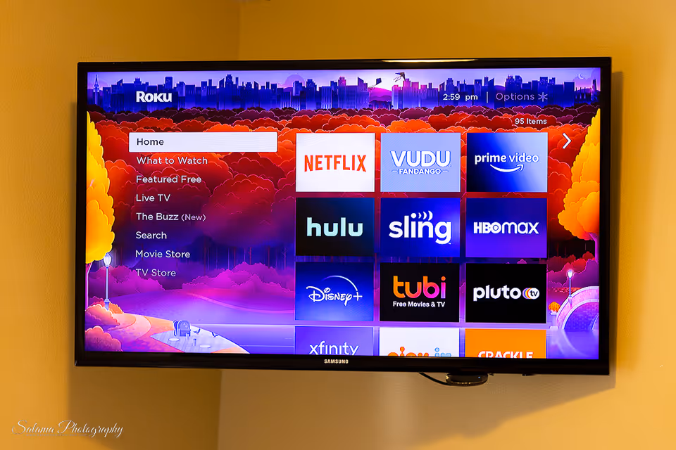 A wall-mounted Samsung TV shows streaming app icons on a yellow wall.