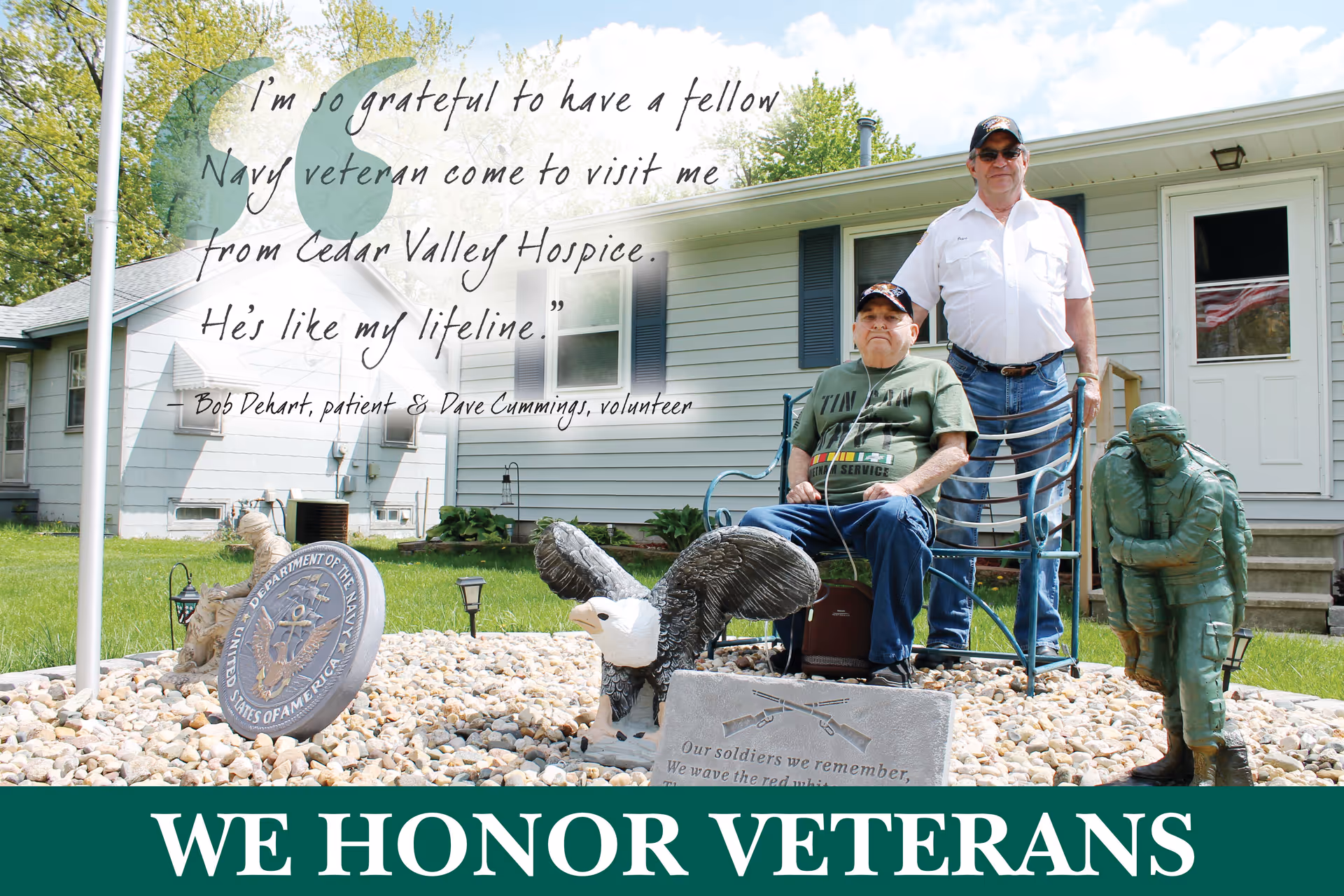 Two men outdoors in front of a house with a veterans statue and banner.