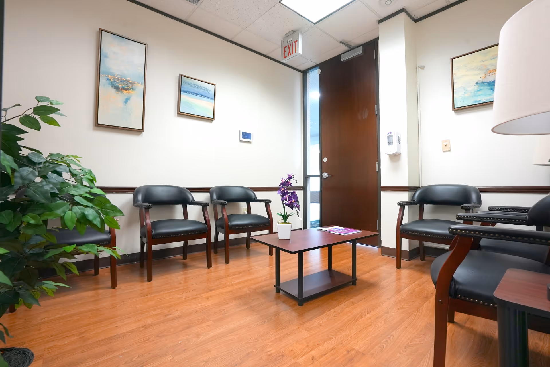 Waiting area with black chairs, a small table, plant, and wall art