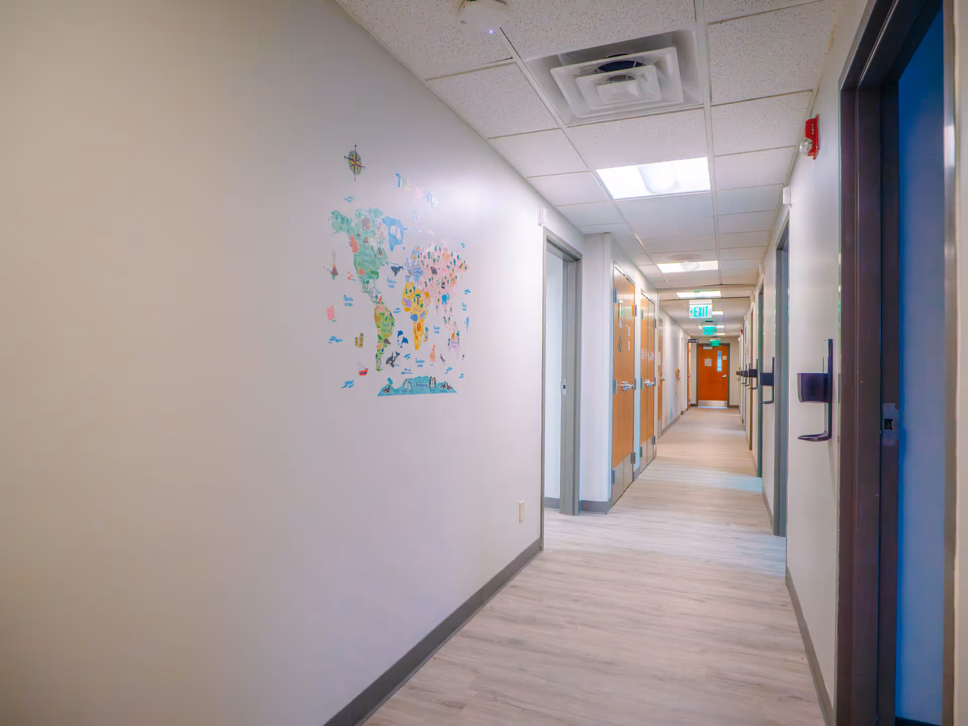 Long, well-lit interior hallway with doors along both sides and a world map mural.