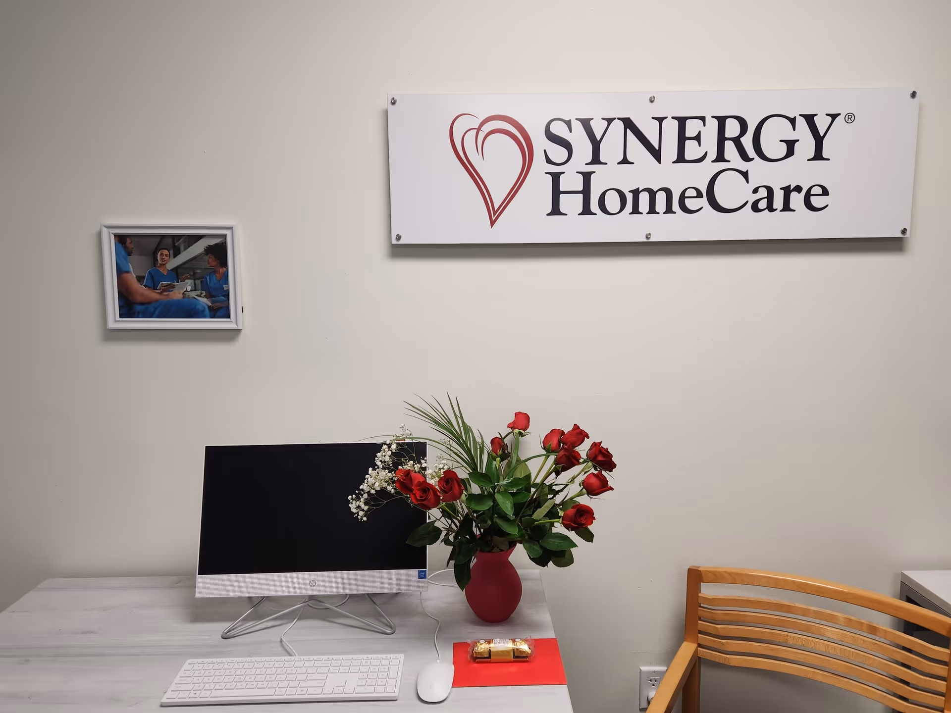 Reception desk with computer, red roses, and a Synergy HomeCare sign on a clean interior wall.