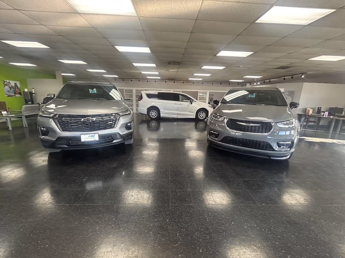 Inside a vehicle showroom with three gray SUVs and a white minivan on display.