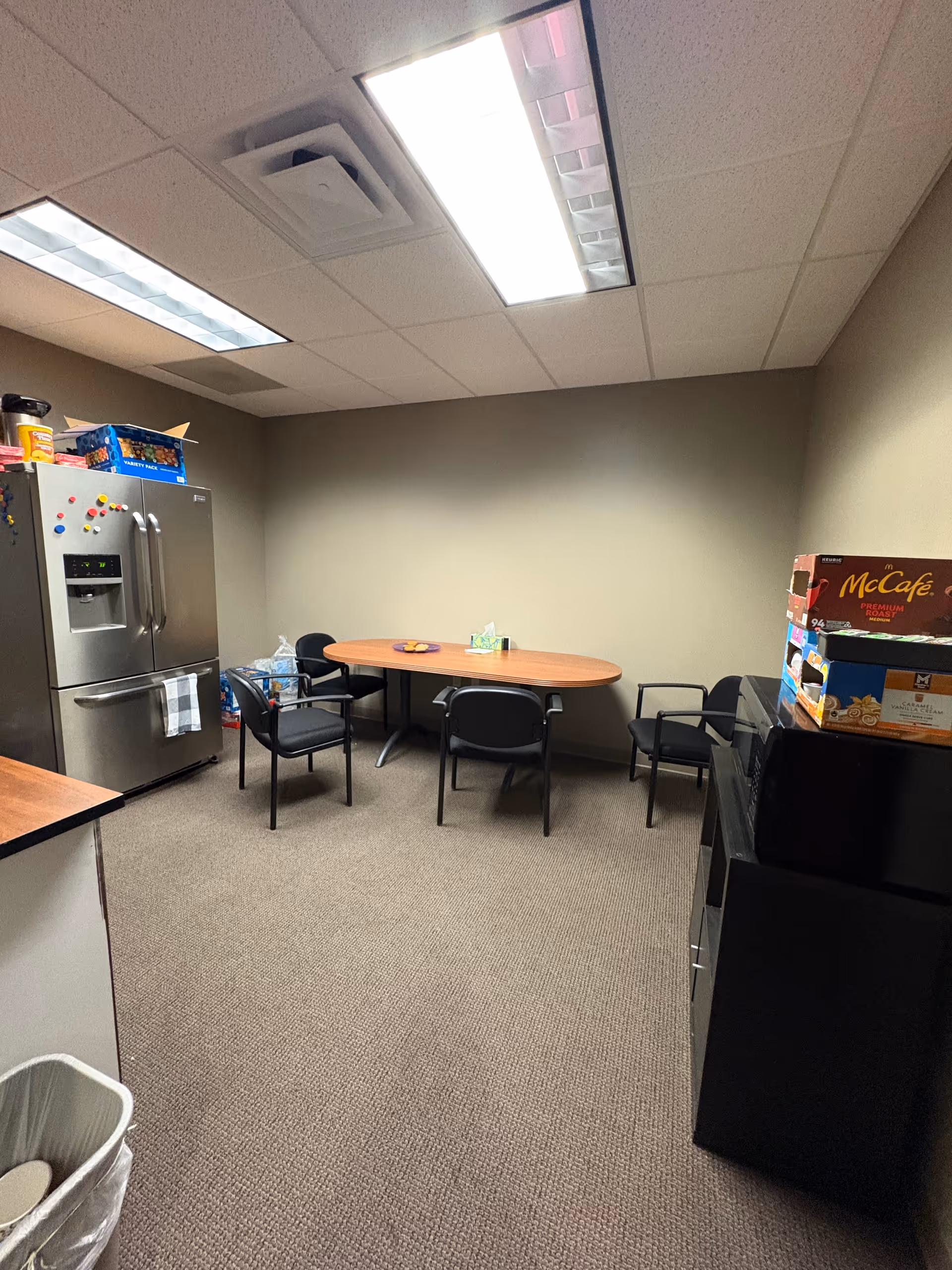 Interior senior living kitchenette with refrigerator, round table, chairs, and snack boxes.