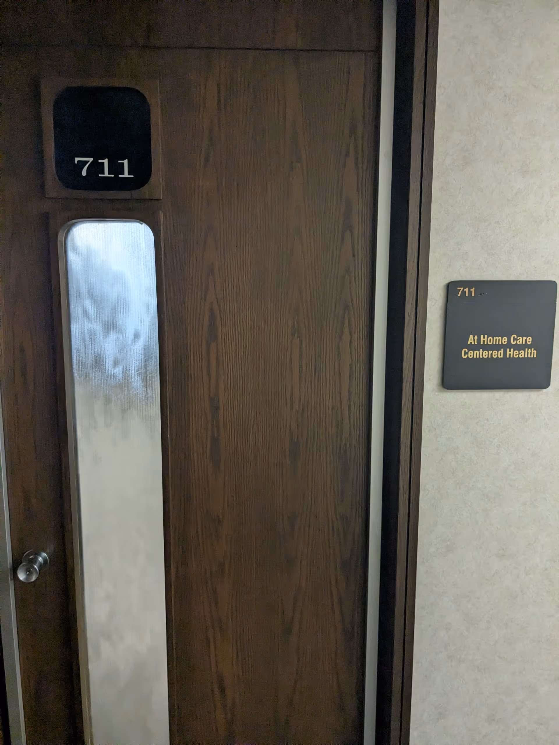 Wooden door marked 711 with wall plaque reading At Home Care Centered Health.
