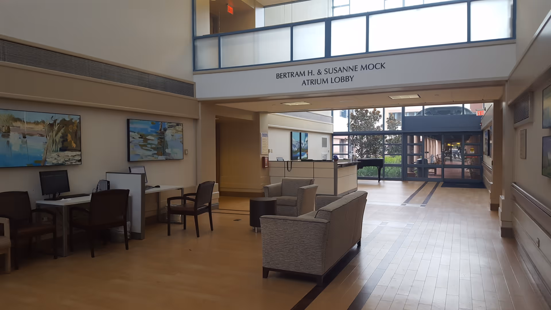 Interior atrium lobby of Miami Jewish Health with seating, computers, and artwork on walls.