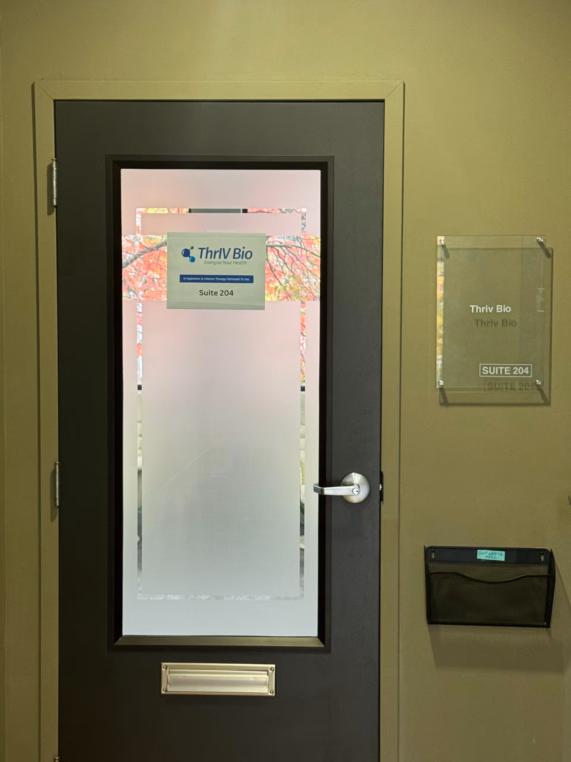A dark interior door with frosted glass labeled ThrIV Bio Suite 204 and hallway signage