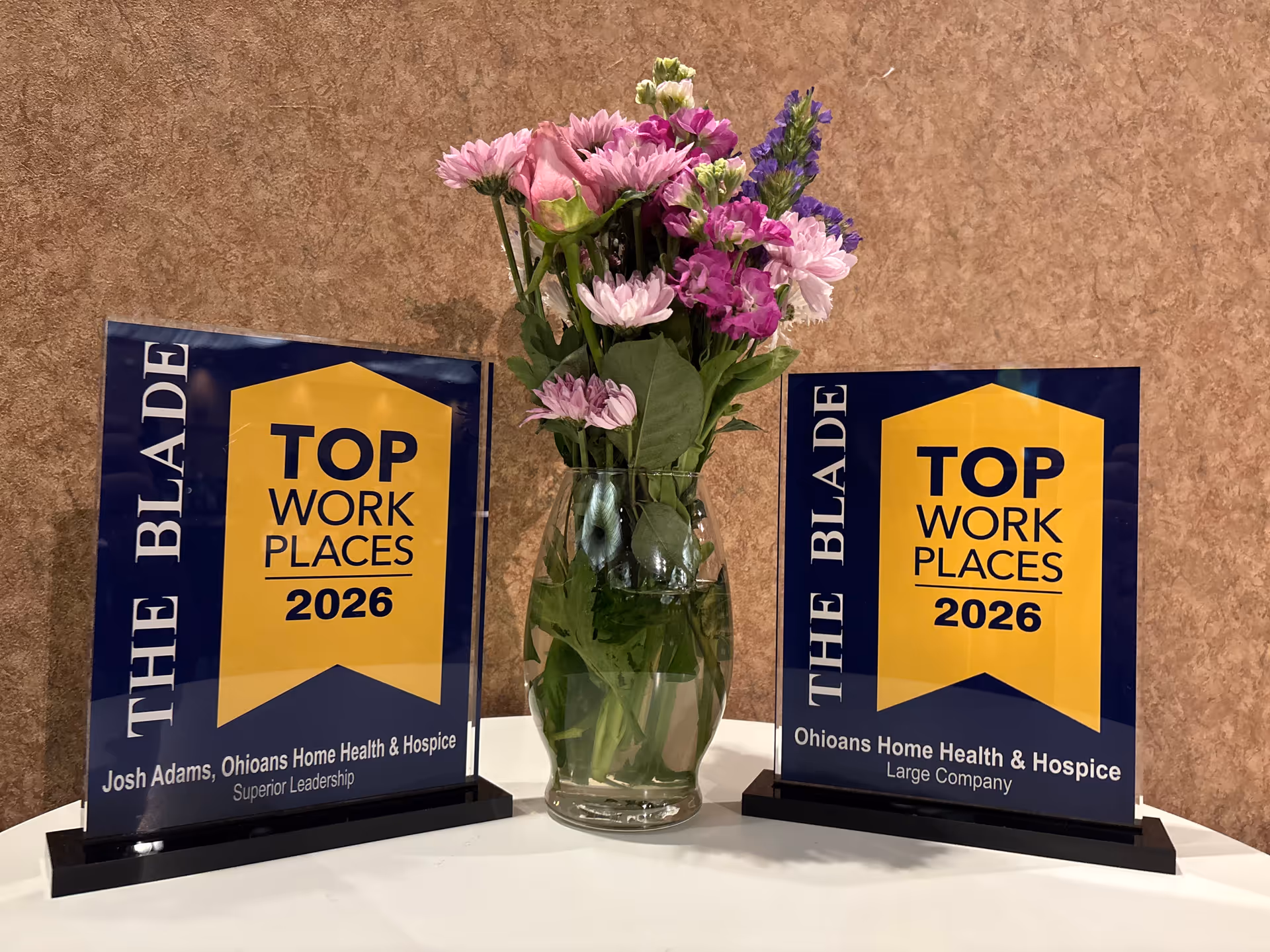 Two award plaques flank a vase of colorful flowers on a white table.