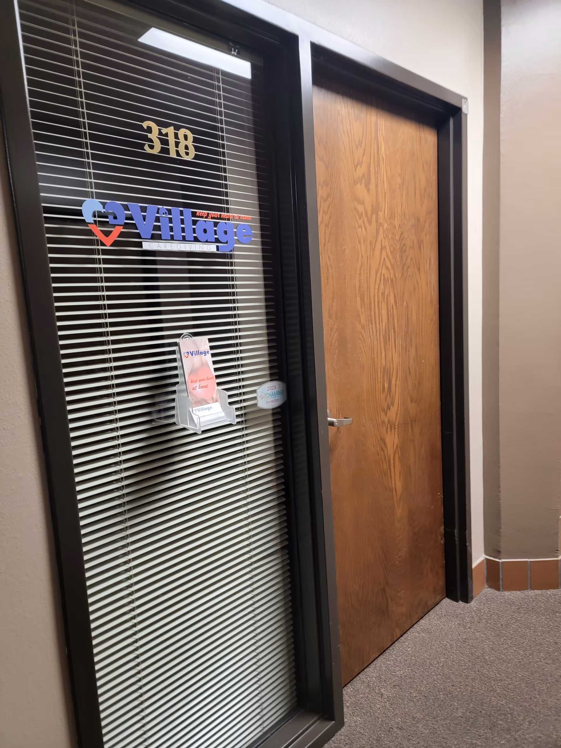 Interior hallway with a glass door displaying Village Caregiving and a wooden door beside it.