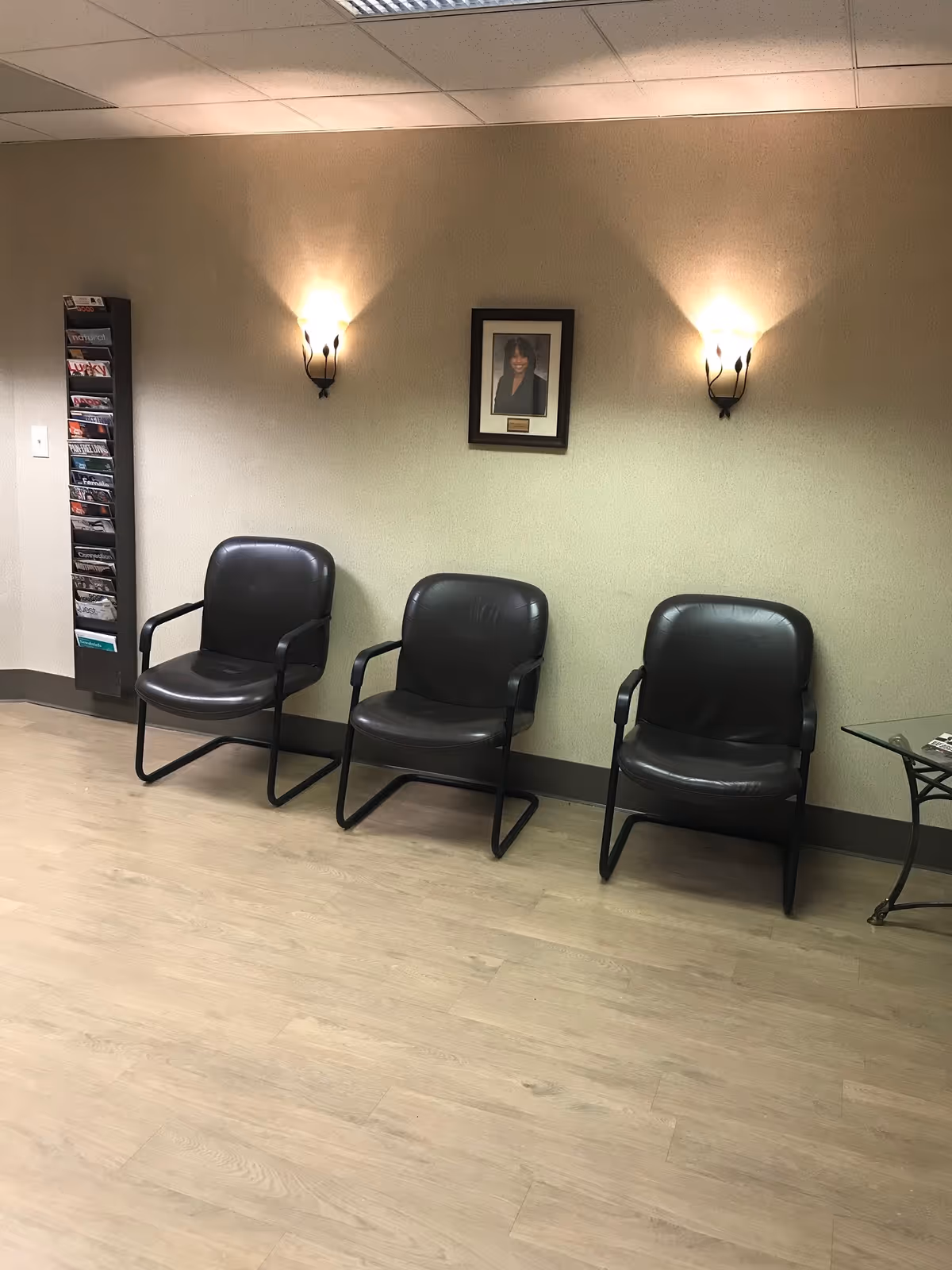 Three black leather chairs line a beige-walled waiting area with sconces and a brochure rack.