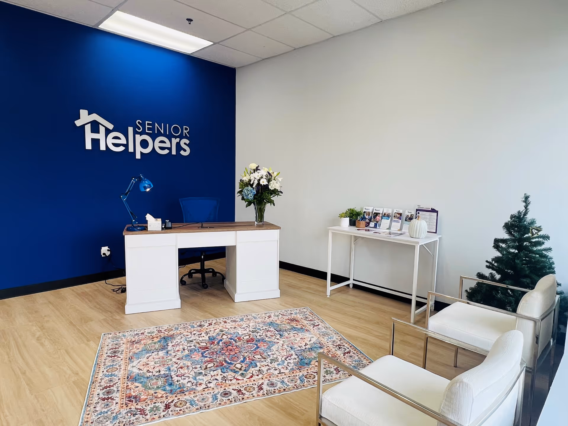 Reception area with Senior Helpers sign, blue wall, desk, brochures, and plants.