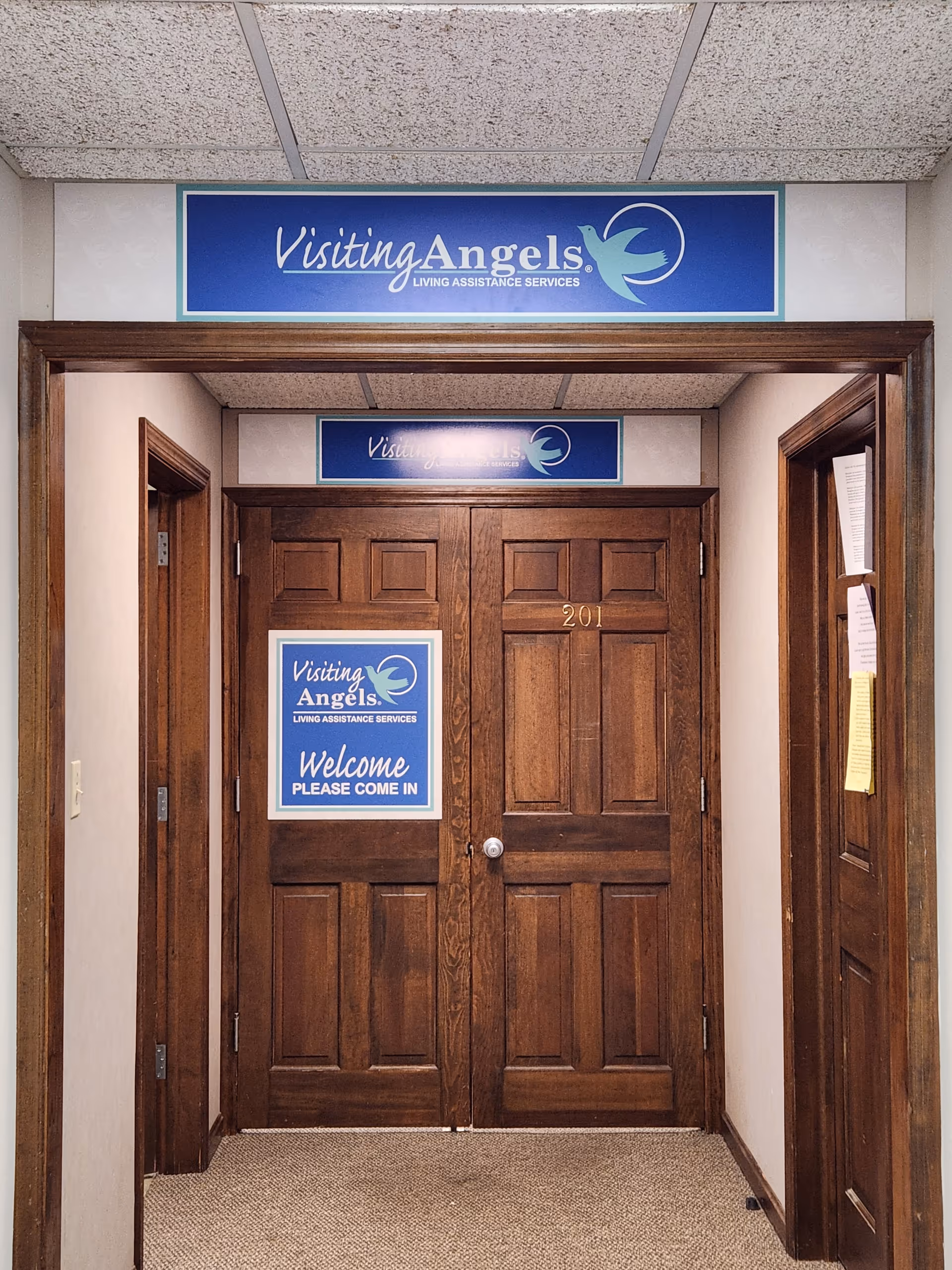 Wood-paneled hallway with double doors and Visiting Angels signage in a senior home.