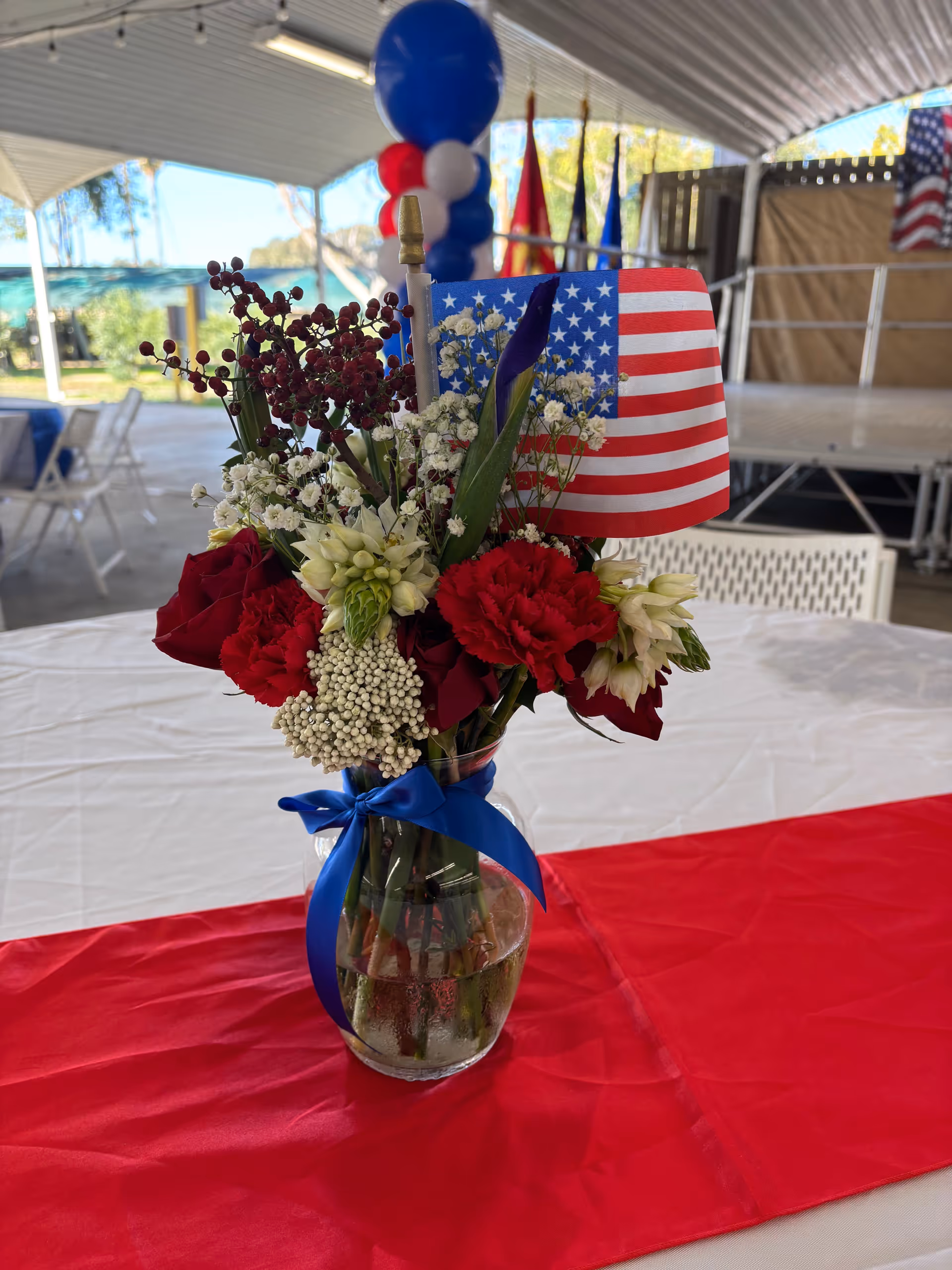 Patriotic floral centerpiece with American flag on a table near a stage.
