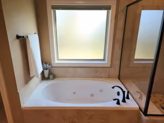 Bathroom with a large soaking tub, tiled surround, towel rack, and frosted window.