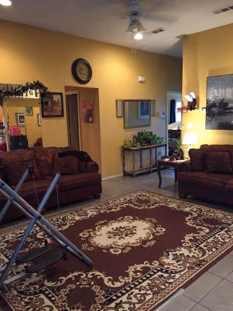 Warm beige living room with two red sofas, ornate rug, plants, and doorway in background.