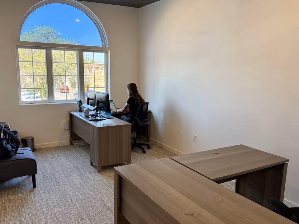 Amada Senior Care interior: desk with computers, a staff member working by a large arched window.