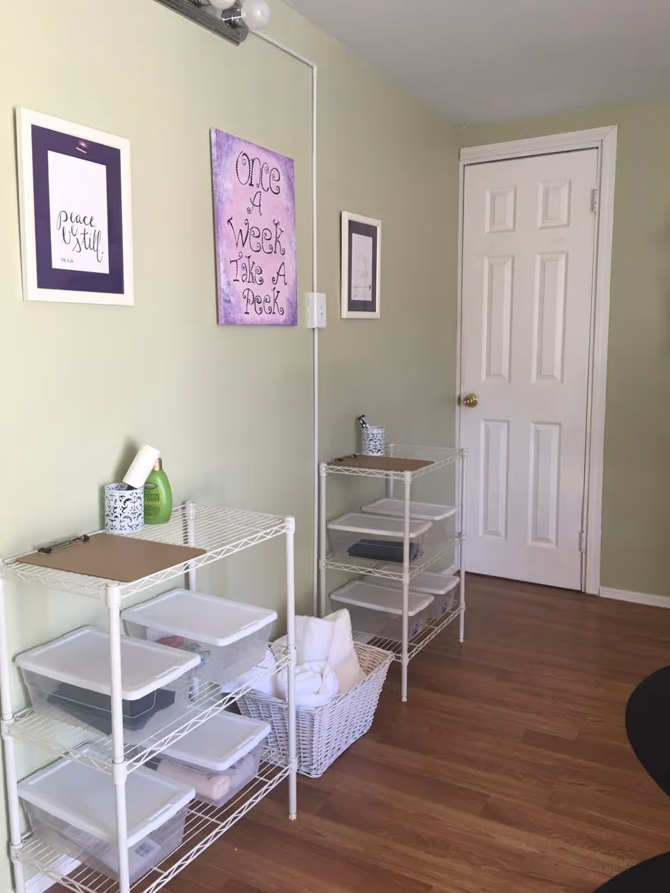 Small interior supply room with white wire shelves, plastic bins, and pastel wall art.