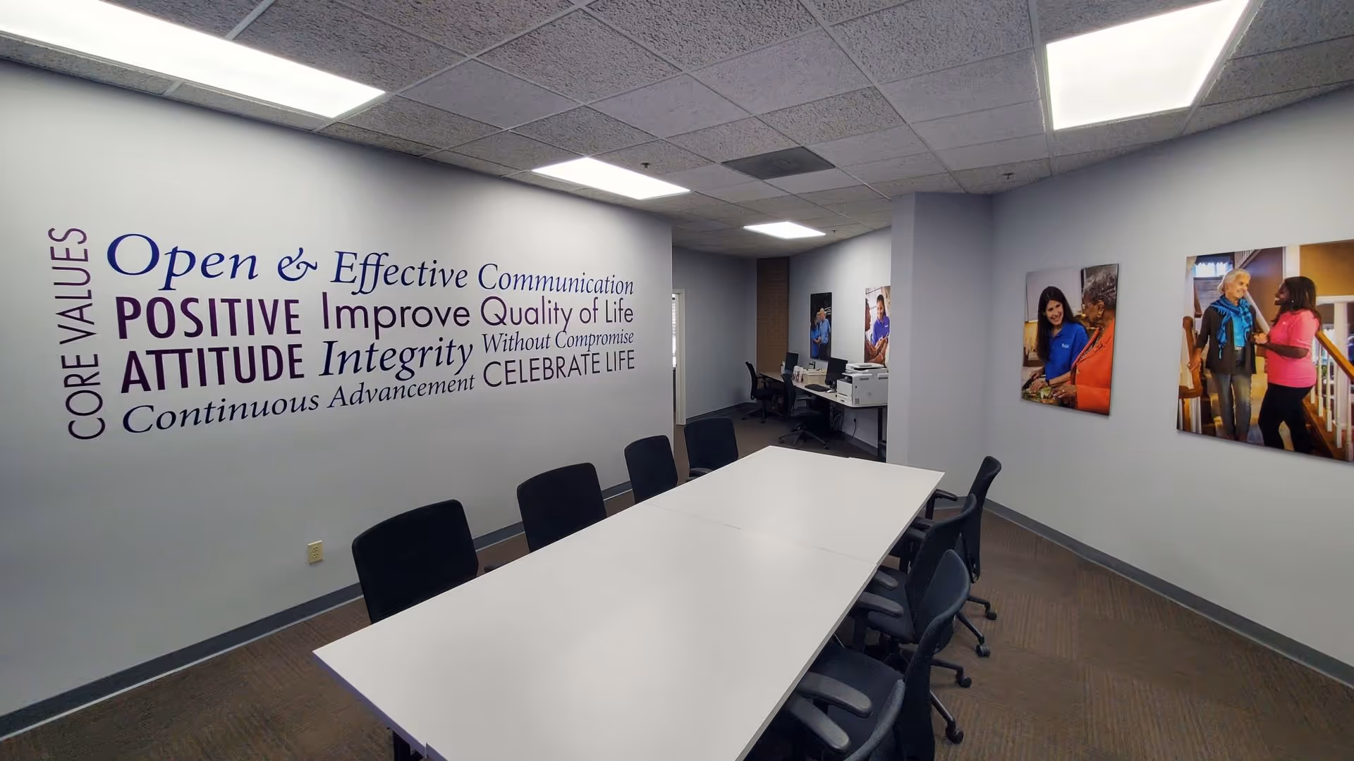 A conference room inside Senior Helpers of Johnson County with a white table and wall art.