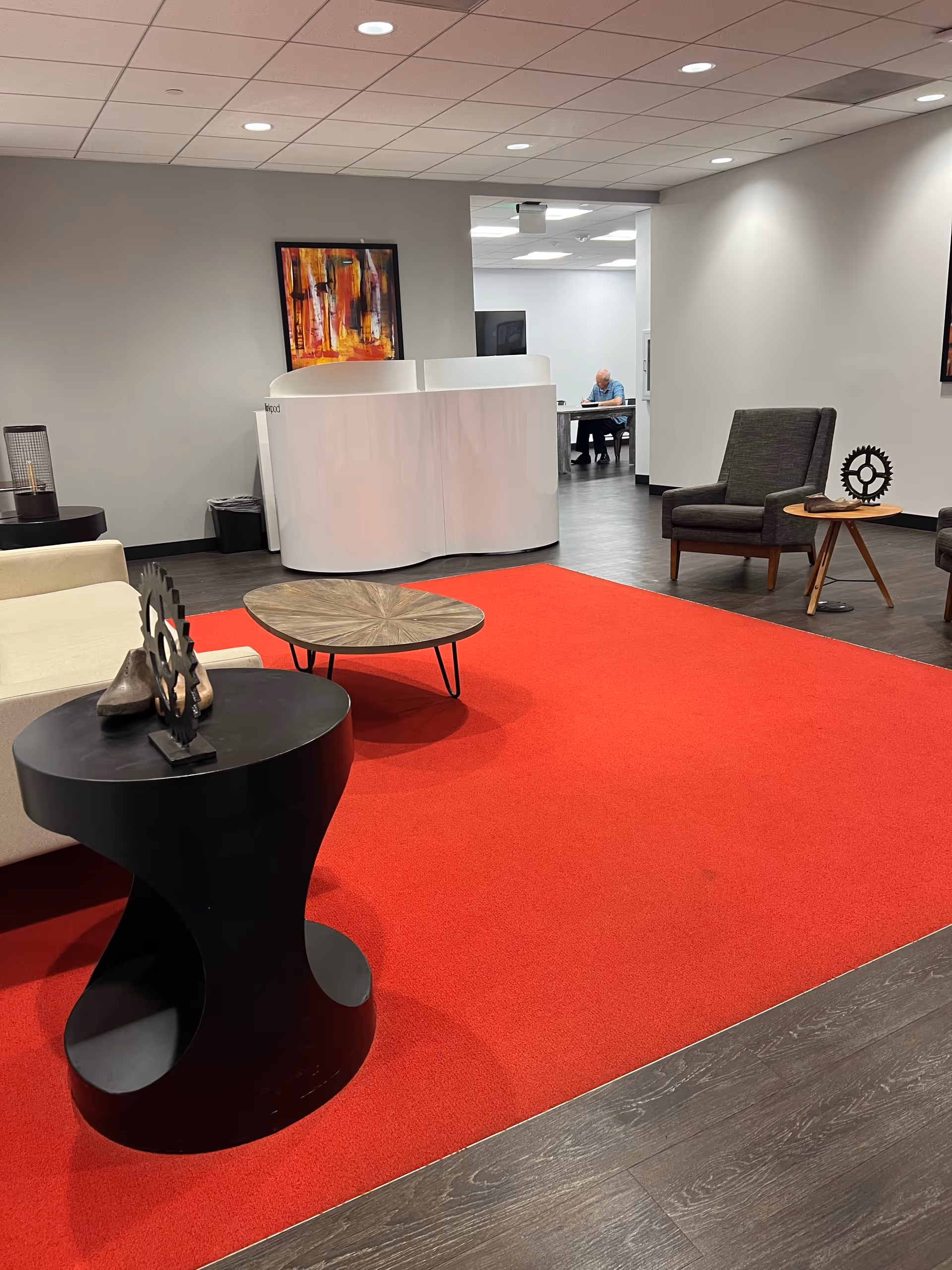 A modern senior living lobby with red carpet, seating, art, and a curved white reception desk.