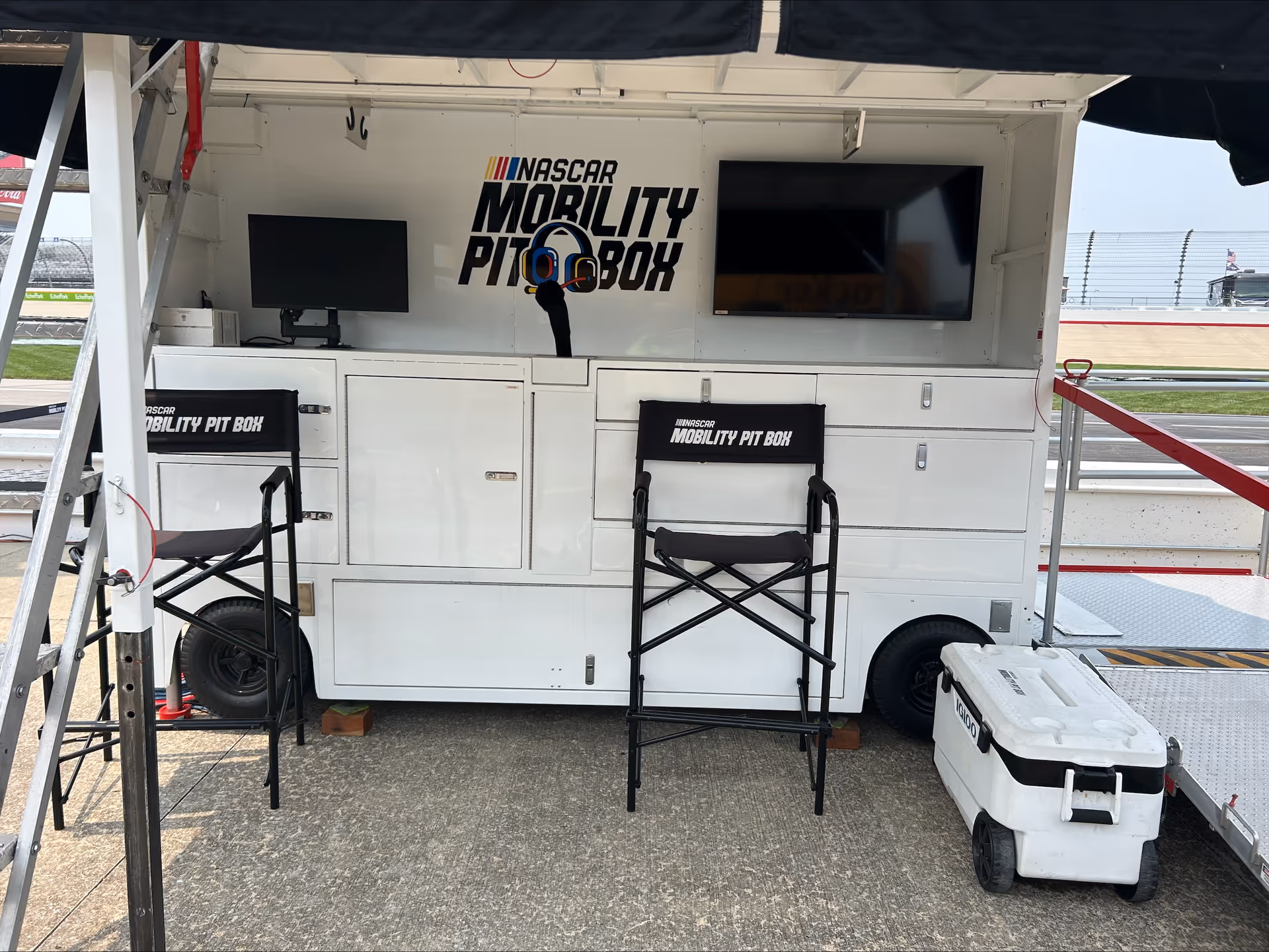 White Mobility Pit Box trailer with two chairs, screens, and a cooler at the race track.