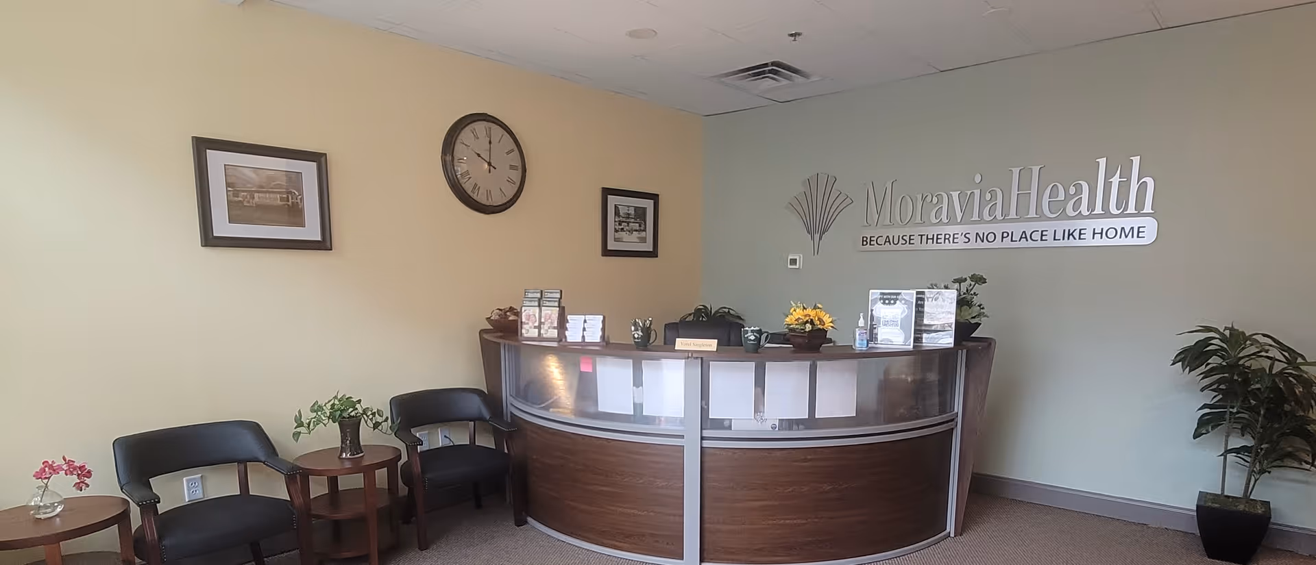 Lobby reception area at MoraviaHealth Harrisburg, with curved desk, chairs, clock, and logo.