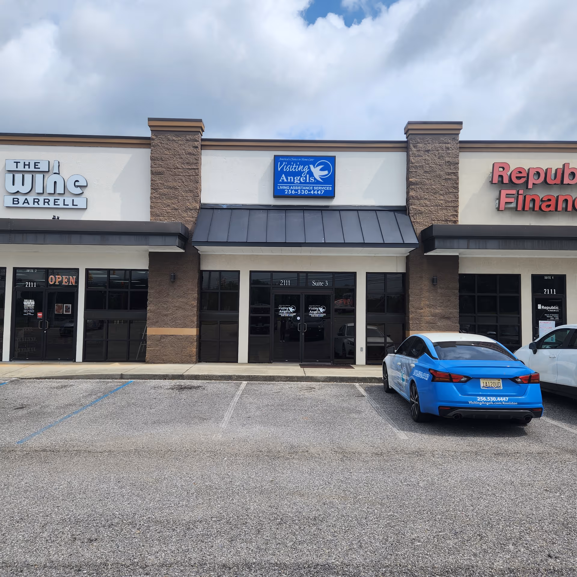 Exterior view of a strip mall storefront with Visiting Angels sign and a blue car.