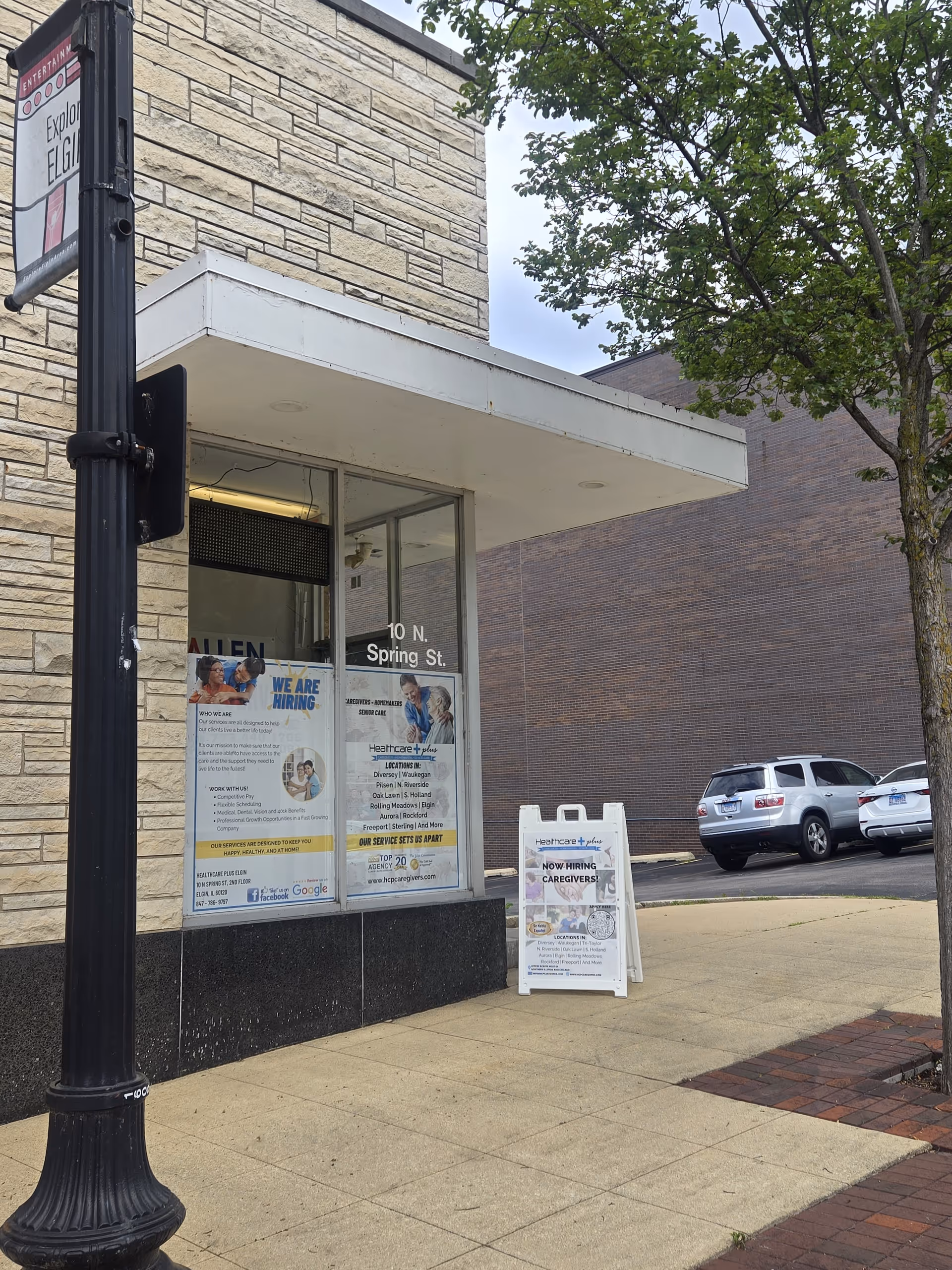 Storefront with 'Healthcare Plus Caregivers' signage, job postings in windows, sidewalk, and parked cars.