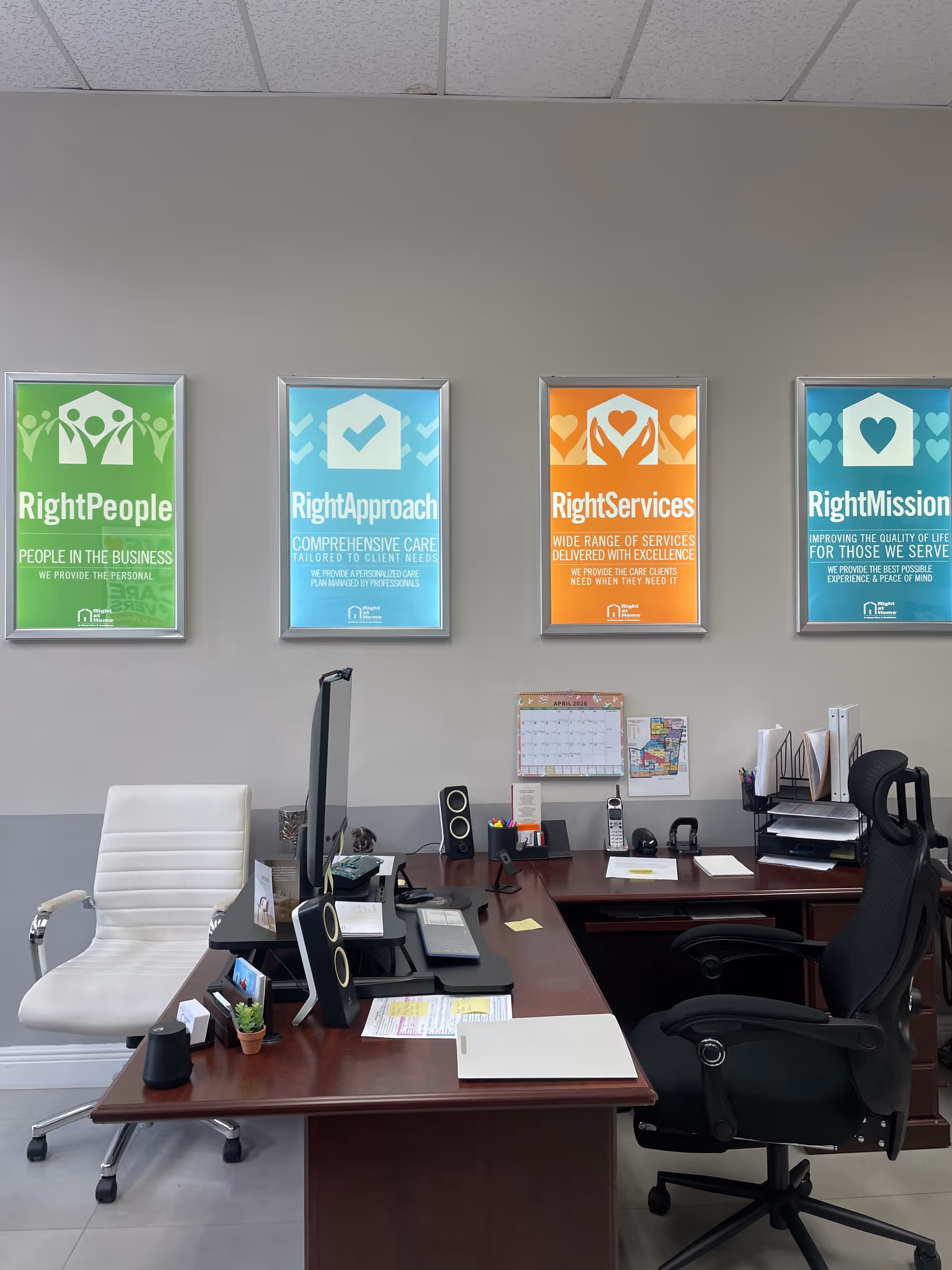 Office reception area with a dark wood desk, white chair, and Right at Home posters.