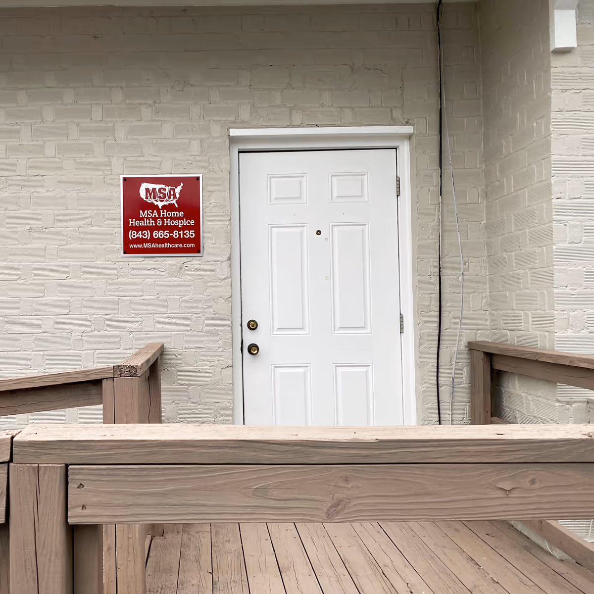 White exterior door in light brick wall with red MSA sign beside it.