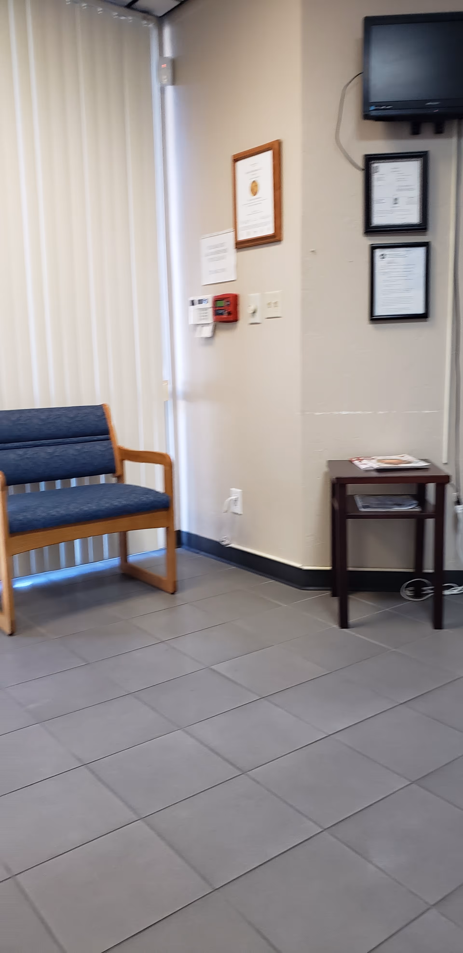 Empty waiting area in a senior facility with a blue chair and wall-mounted certificates.
