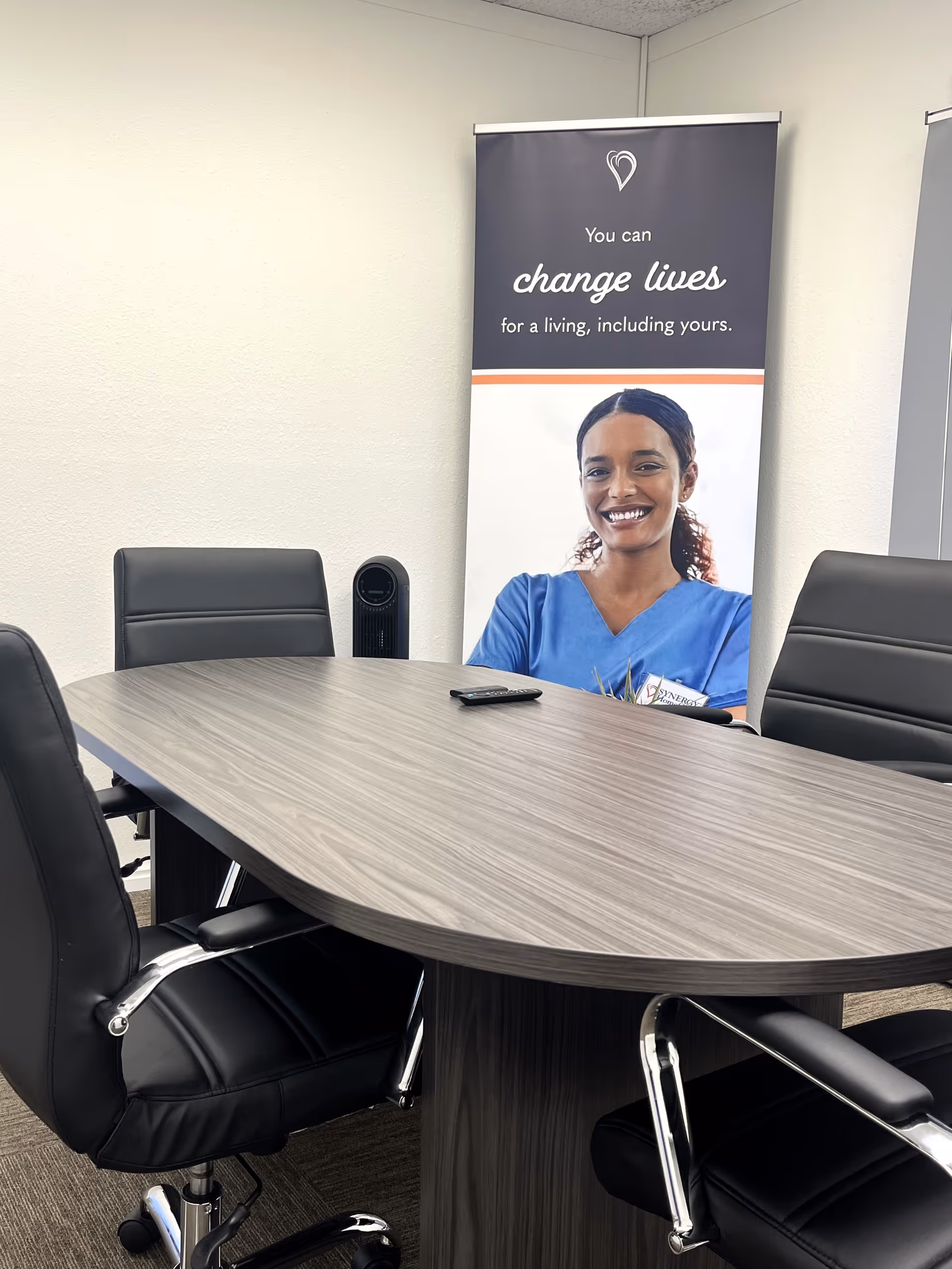 Conference room with oval table, black chairs, and a Synergy HomeCare banner.