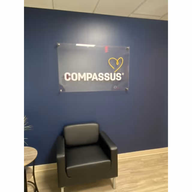 Blue wall features a Compassus sign and a black leather chair in a reception area.