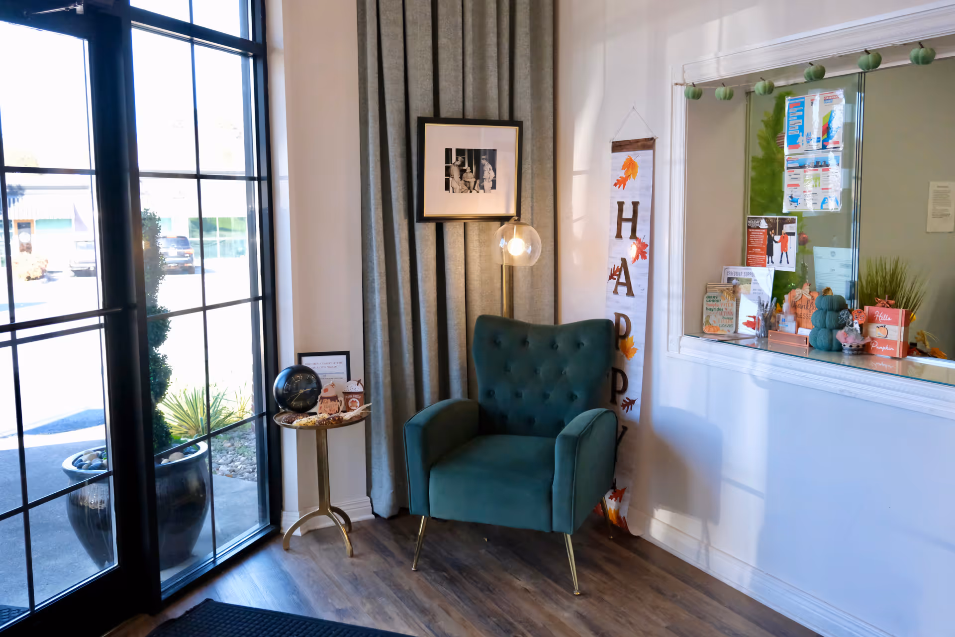 Teal armchair beside a glass entrance, small side table, and decorative wall in a lobby.