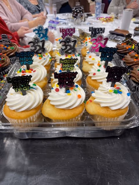 A tray of cupcakes with white frosting and Happy New Year toppers sits on a table.
