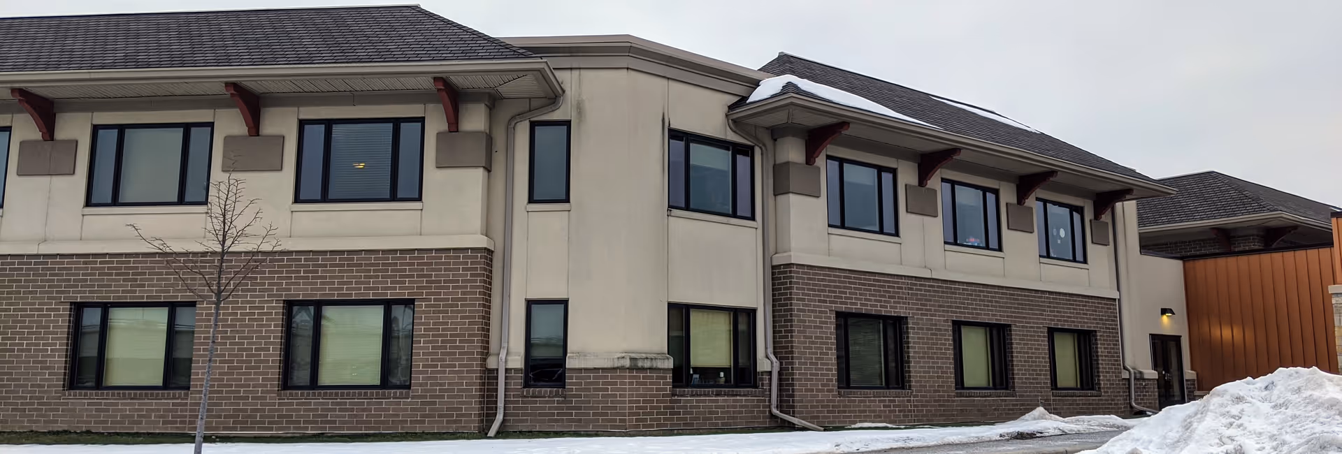 Exterior view of a two-story beige brick-and-plaster senior housing facility in snow.