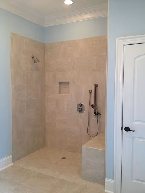 Beige tiled walk-in shower with niche and handheld shower in a blue bathroom.