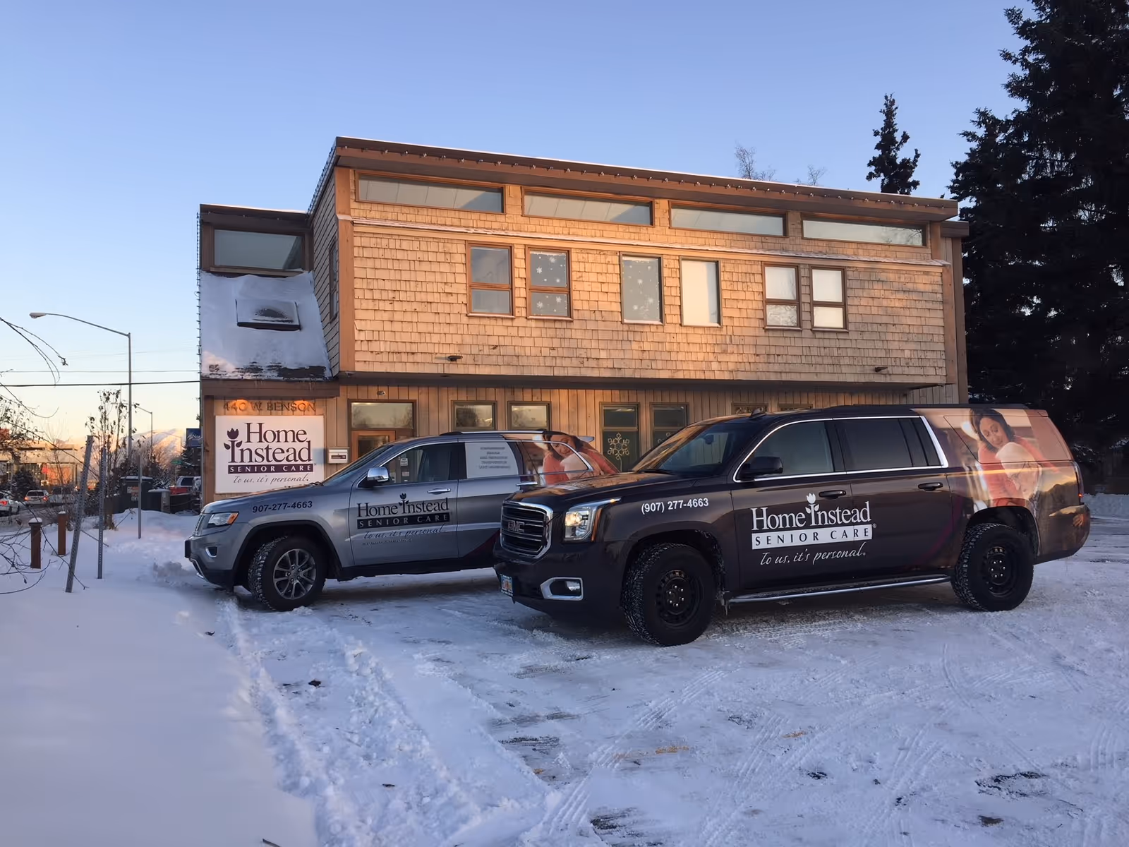 Two Home Instead vans parked in snow outside a wooden two-story senior care building.