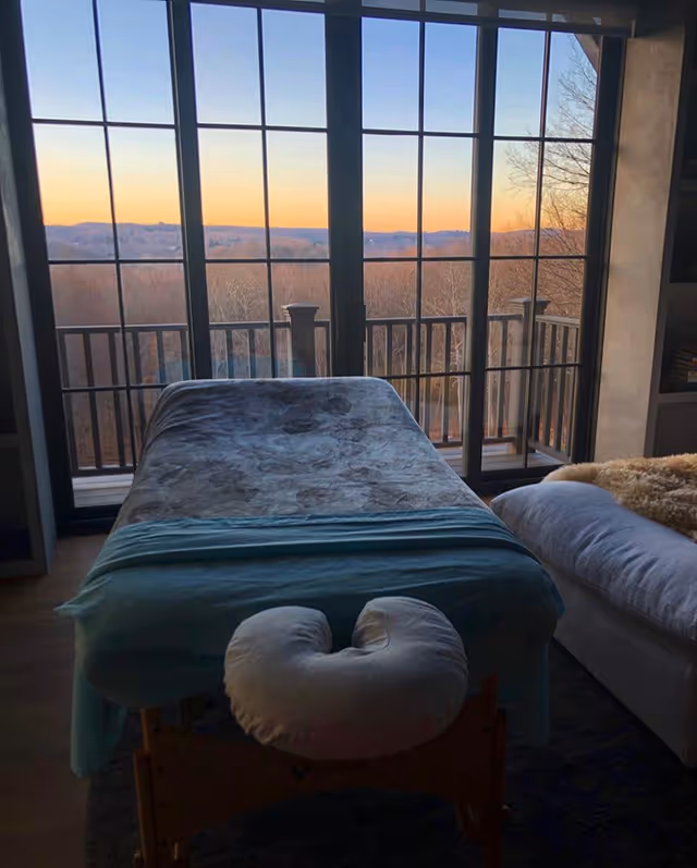 Private treatment room with massage table and large window balcony view.